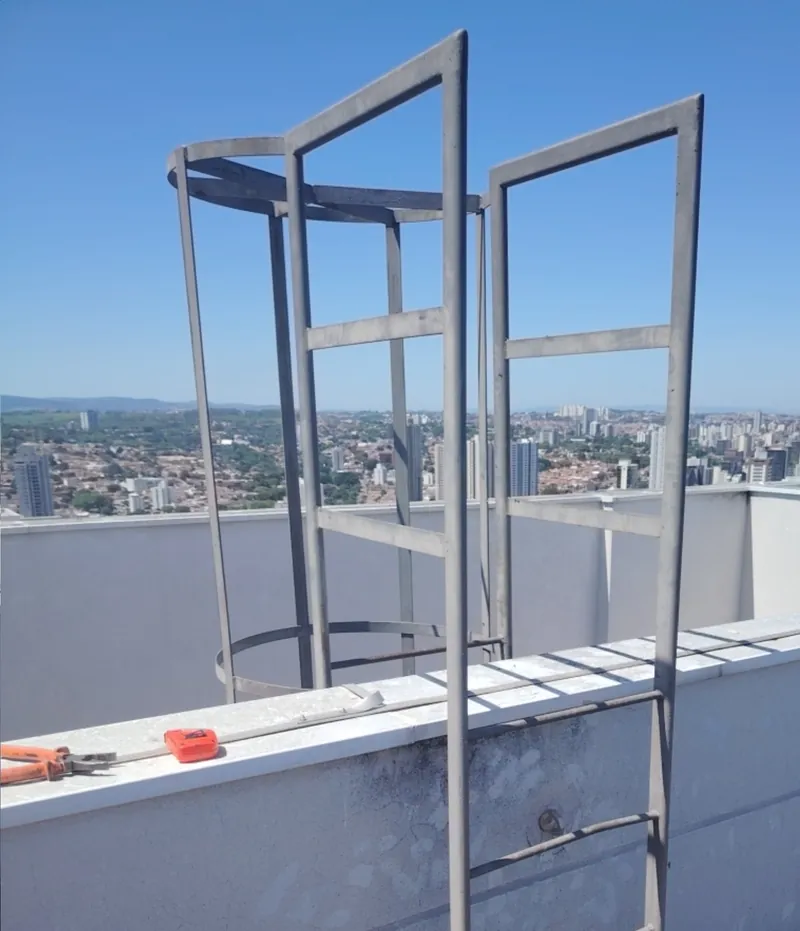 Escada tipo marinheiro com guarda-corpo no topo de um edifício, com a cidade ao fundo