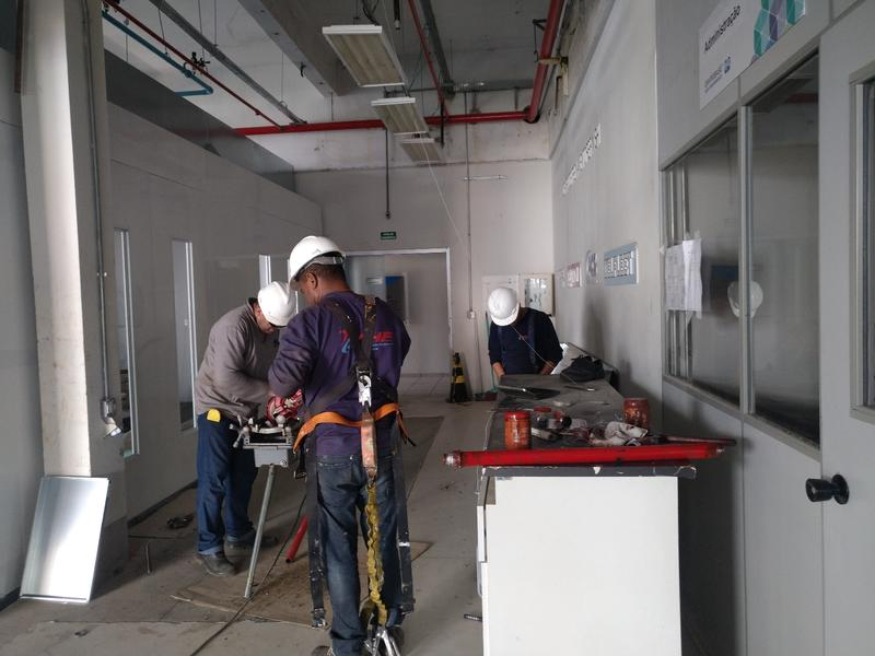 Colaboradores durante os trabalhos no interior da cabine de pintura, com tubulação de sprinklers acima